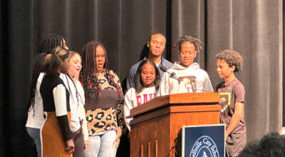 PHOTO BY MARÍA CAMP - Aaron Freeman directs Russellville Middle School Students in singing the national anthem as part of the annual Russellville City Schools Black History Month program.  